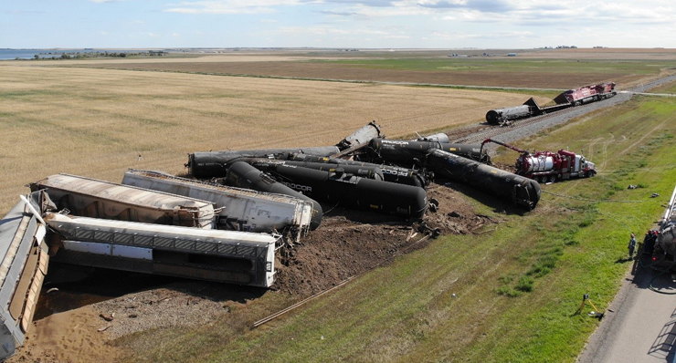 Train derailment near a road in a treeless prairie.