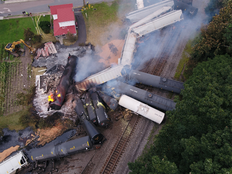 Overhead shot of several freight cars derailed and burning.