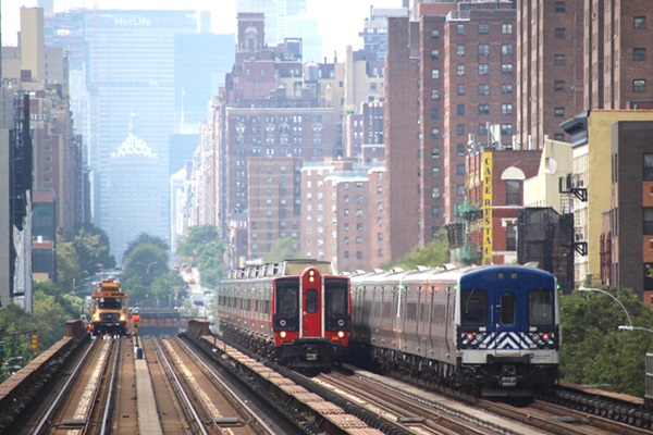 Electric multiple unit commuter trains on four-track main line with New York skyline as backdrop
