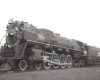 An oblique front view of a 4-8-2 steam locomotive in a rail yard.