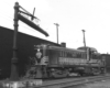 An early diesel locomotive pauses in a freight yard near a water standpipe.