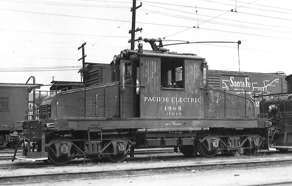 A steeple cab electric freight motor surrounded by other freight equipment.