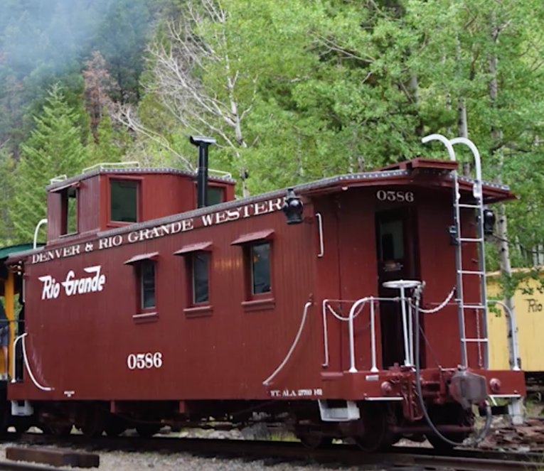 Freshly painted caboose in mountain scenery.