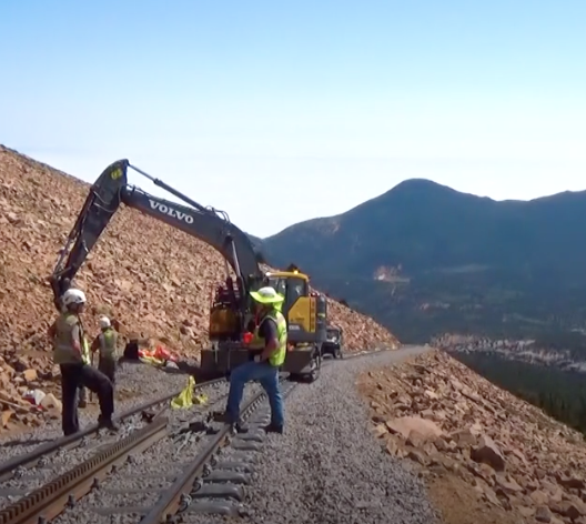 Track workers and a back hoe work high on a mountain top.