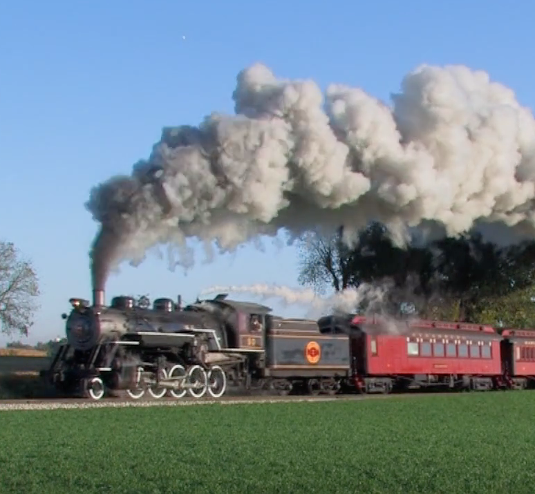 Steam locomotive hauling a passenger train under a clear sky.