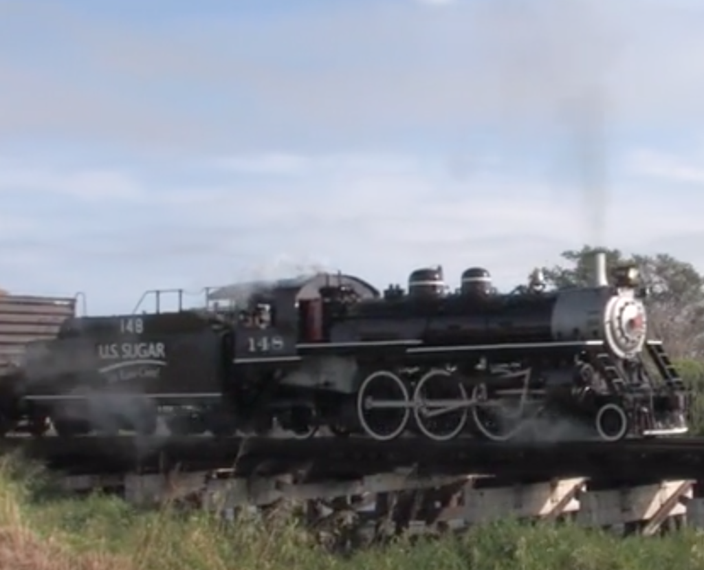 Steam locomotive hauls freight train over bridge.