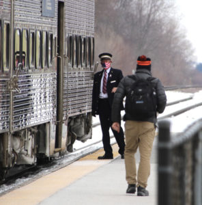 Conductor with mask waits by passenger train