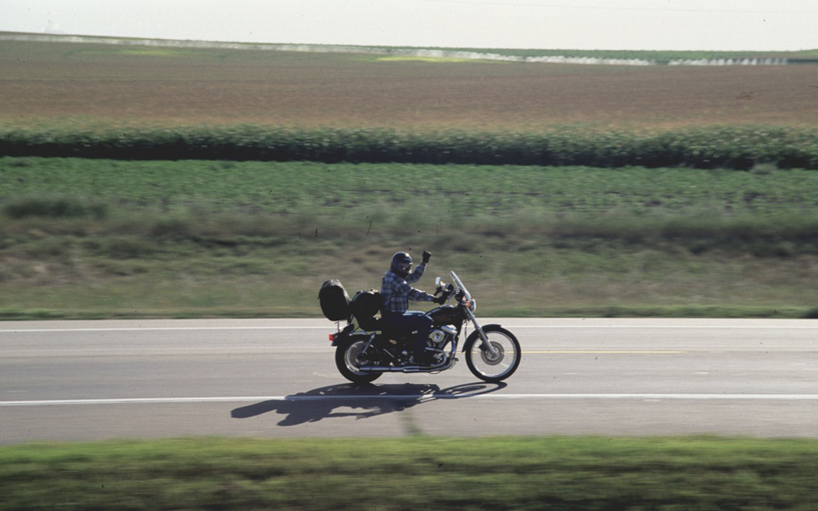 Motorcycle rider waiving while driving.