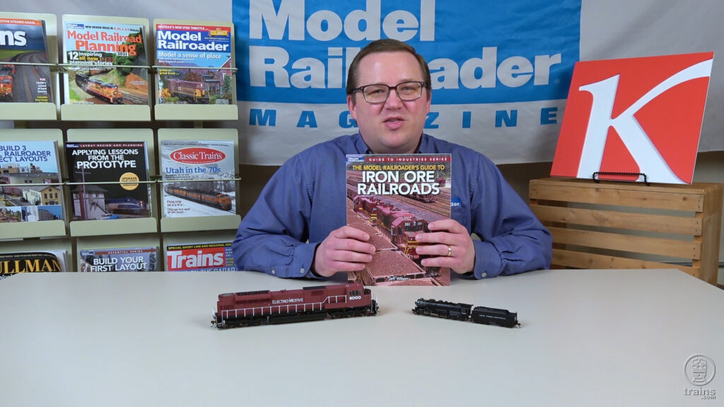 Man holding book at table with model trains.