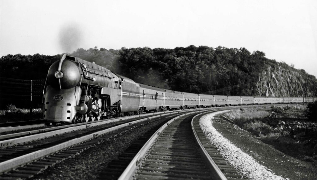 Streamlined steam locomotive leading a streamline passenger train on a gentle curve.