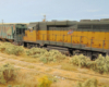 : A rusty yellow-and-green diesel and a worn green covered hopper roll down an equally neglected spur track on the prairie
