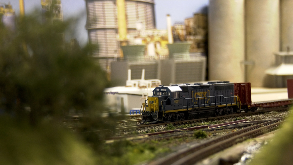 A CSX train sits in the middle of a track, the scene is partially covered by a bush