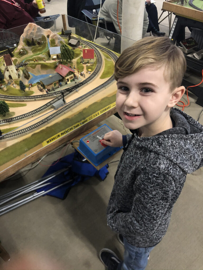 Gabriel Turlan stands in front of a model layout, running the trains