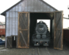 The nose of a steam locomotive is seen through the door of a single-stall wooden engine house