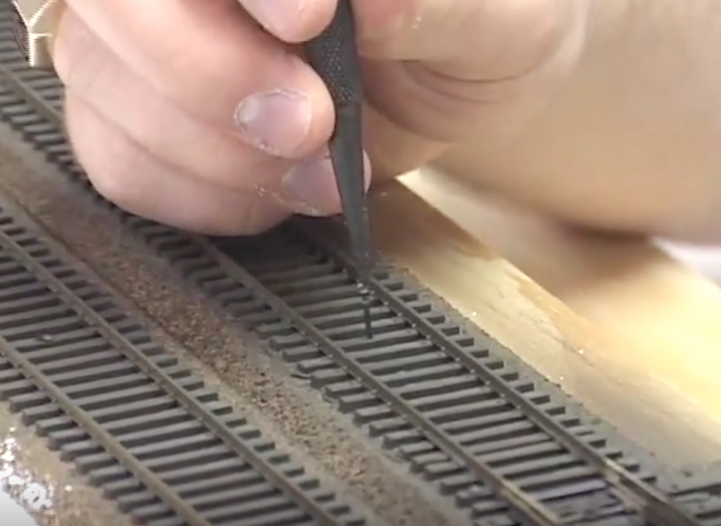 Caucasian hand holding nail punch over unfinished model track work.