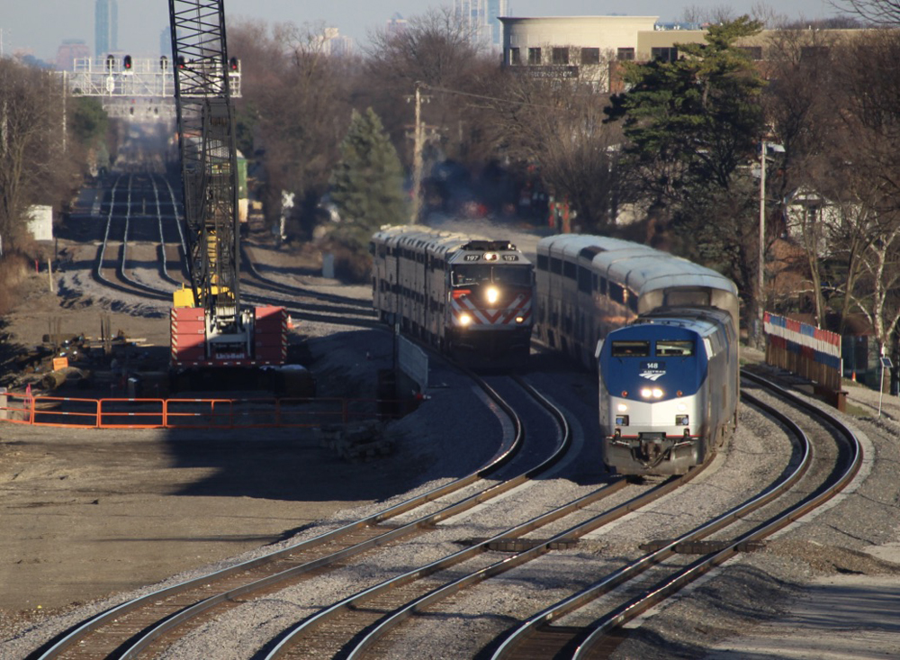 Amtrak passenger train passes Metra commuter train in view from bridge across tracks.
