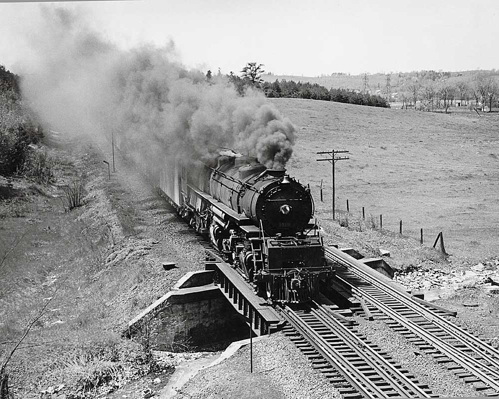 Smoking steam locomotive crosses short bridge with train