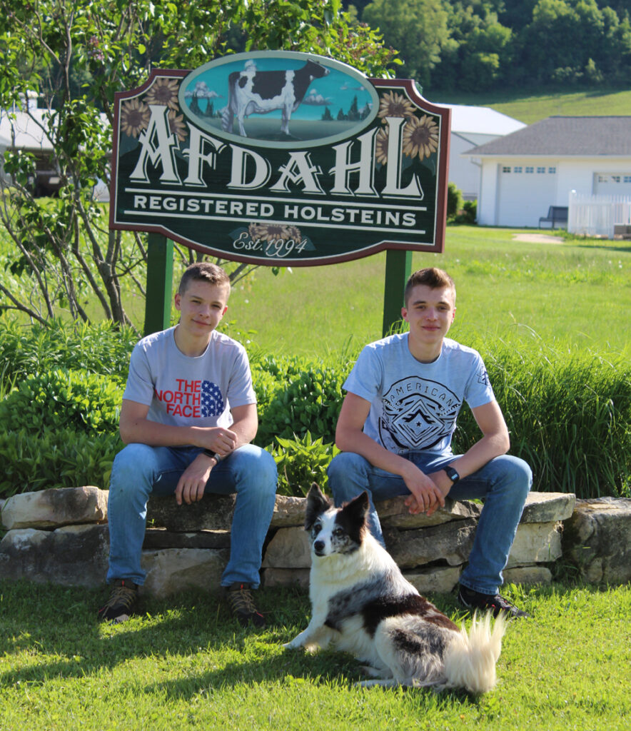 Bo and Ian Afdahl sit in front of an Afdahl Farm sign.