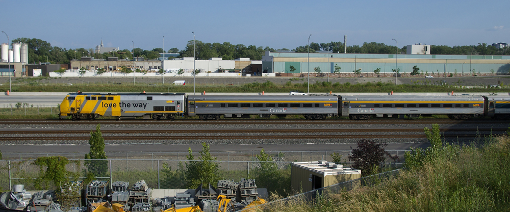 Silver and yellow locomotive followed by stainless steel cars