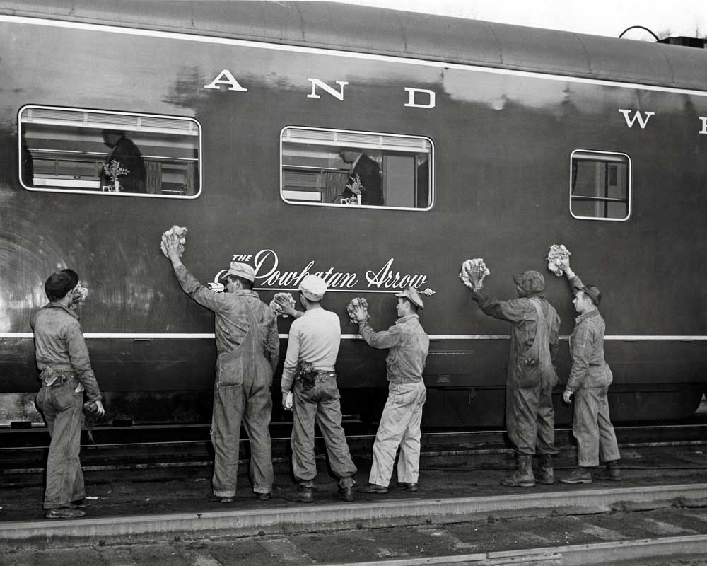Workers stand beside streamlined passenger rail car