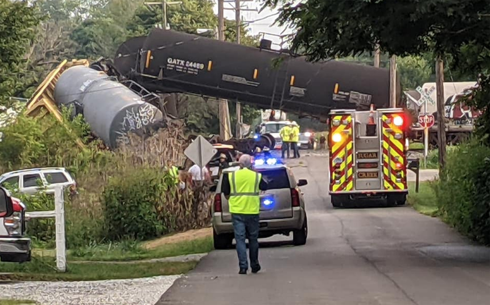 Derailed cars, including tank car lifted above roadway