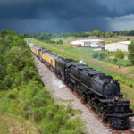 Large black steam locomotive with train against a dark blue sky.