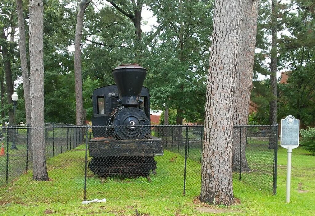 Steam locomotive displayed behind fence among trees