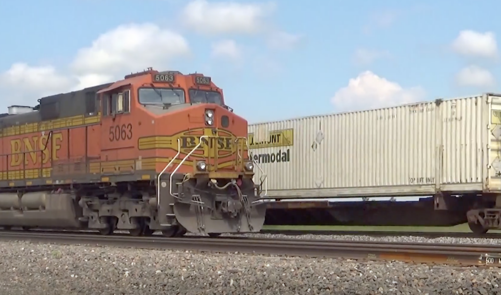 An orange freight locomotive stopped at a siding passed by a freight train.