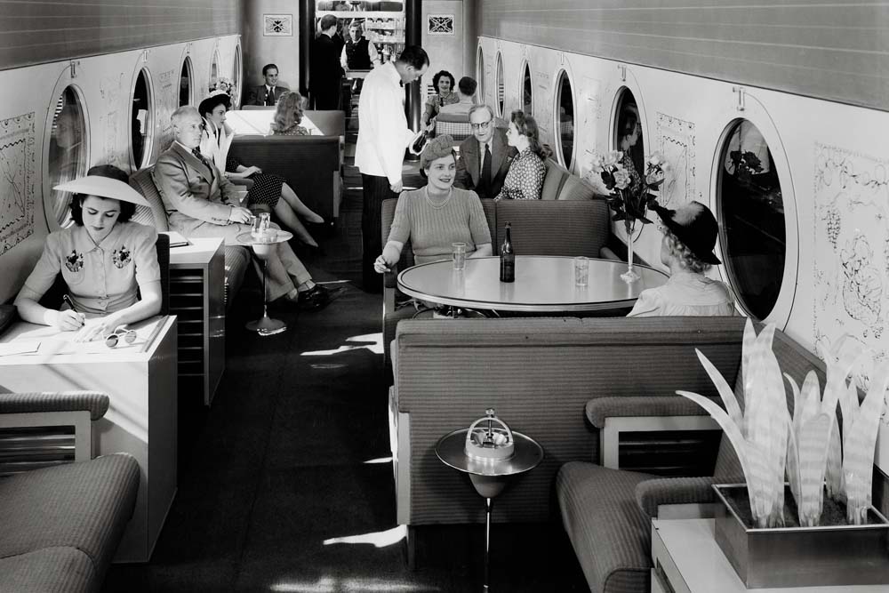 People seated in railroad lounge car with porthole windows