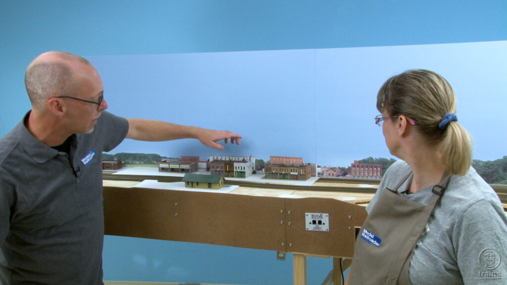 David Popp talking to Rene Schweitzer while pointing to the backdrop on a model railroad