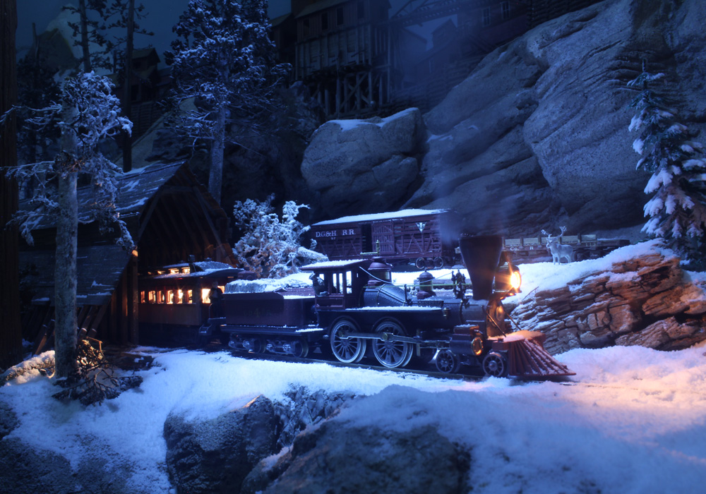 A steam locomotive leads a passenger car from a snow shed in a moonlit winter scene