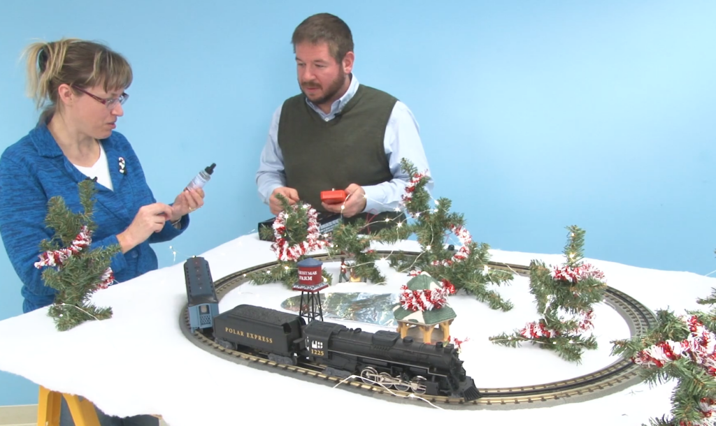 Two people behind a small winter-themed toy train layout.