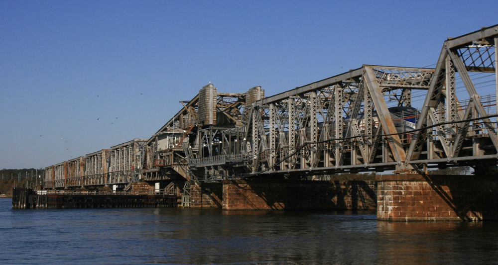 Passenger train barely visible through girders of steel bridge