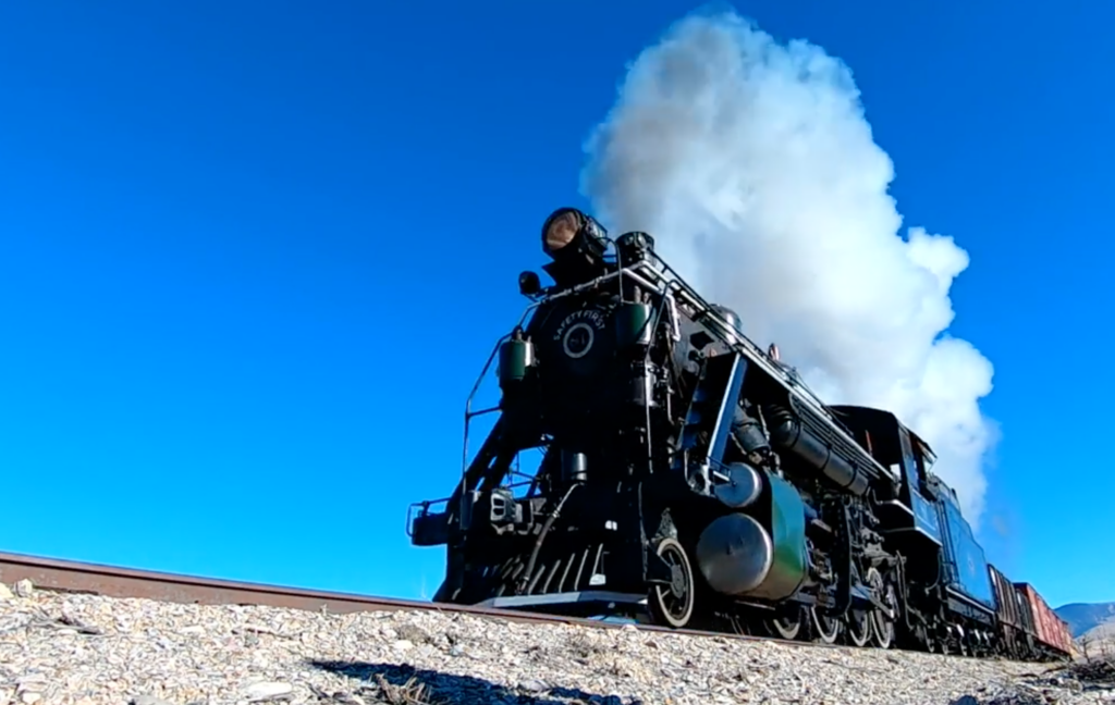 Steam locomotive with white smoke plume seen from a low angle.