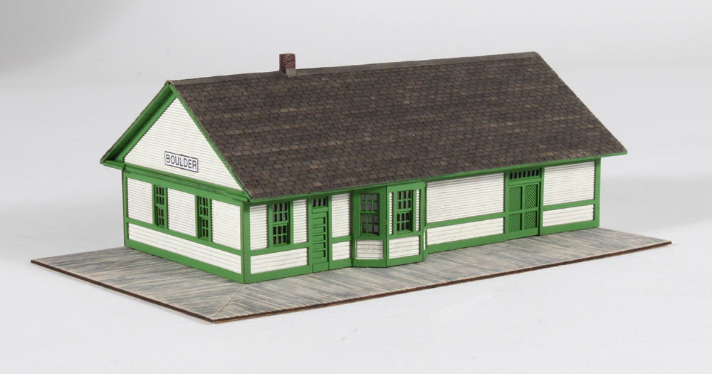 Laser-cut wood combination depot painted green and white with gray three-tab shingles.