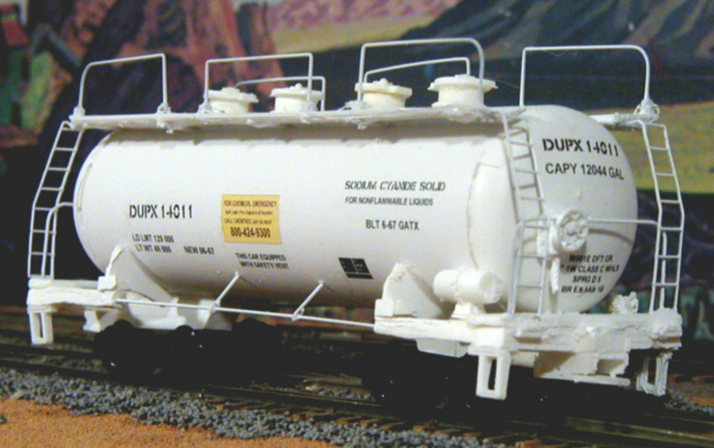 Photo of HO scale tank car painted white with yellow and black graphics on scenicked base.