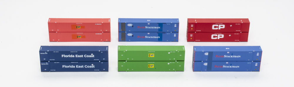 Photograph of 12 N scale intermodal containers in various paint schemes on white background.
