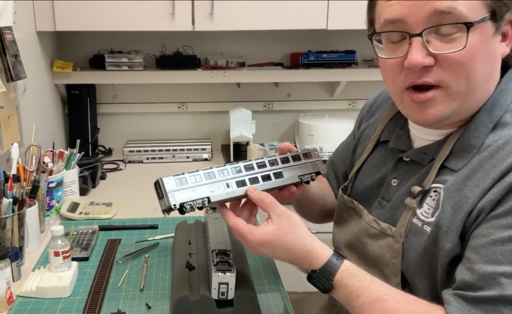 Man holding a silvery passenger car at a work table.