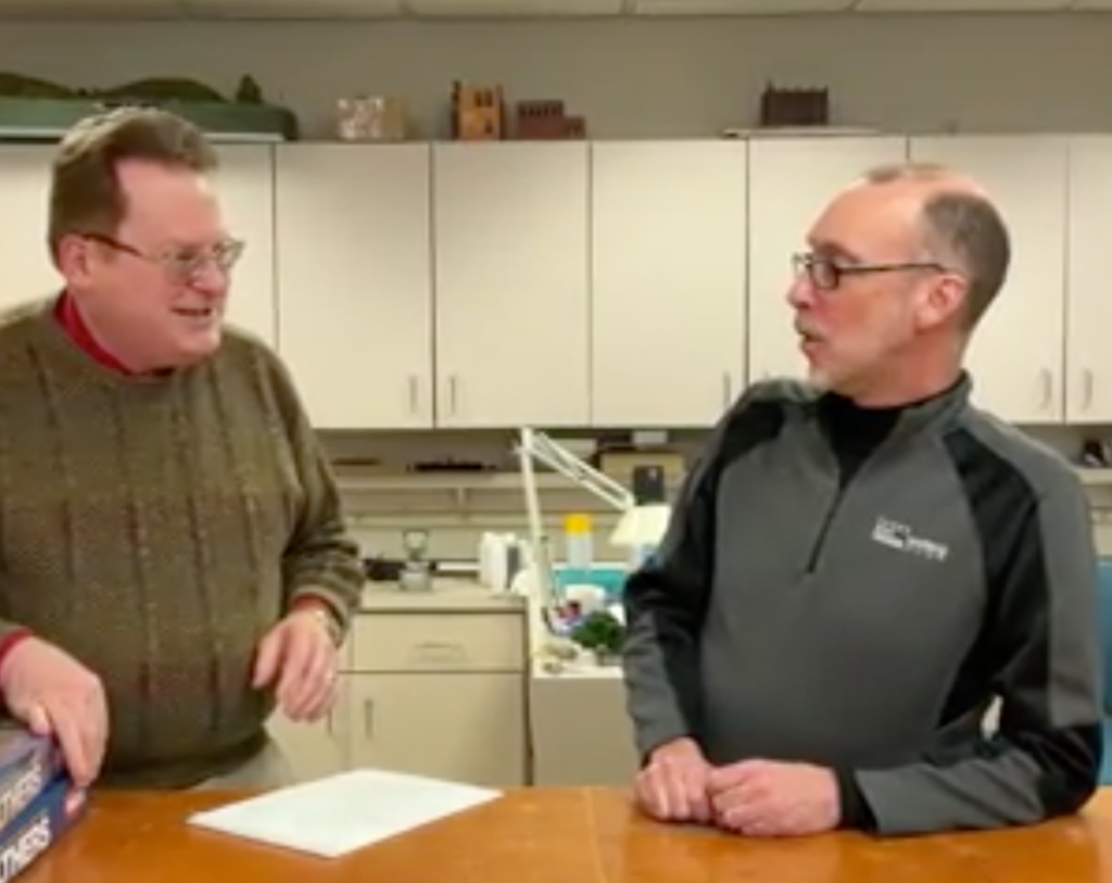 Two men at a workbench talking.