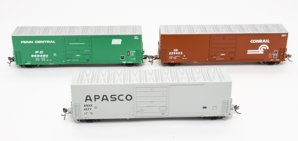 Photo of three HO scale boxcars on white background, one each painted Deepwater Green, brown, and gray.