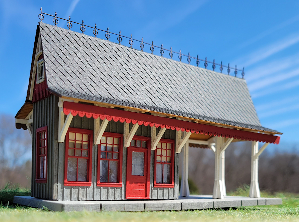 Photo of HO scale station painted gray, red, and white with gray diamond shingles.