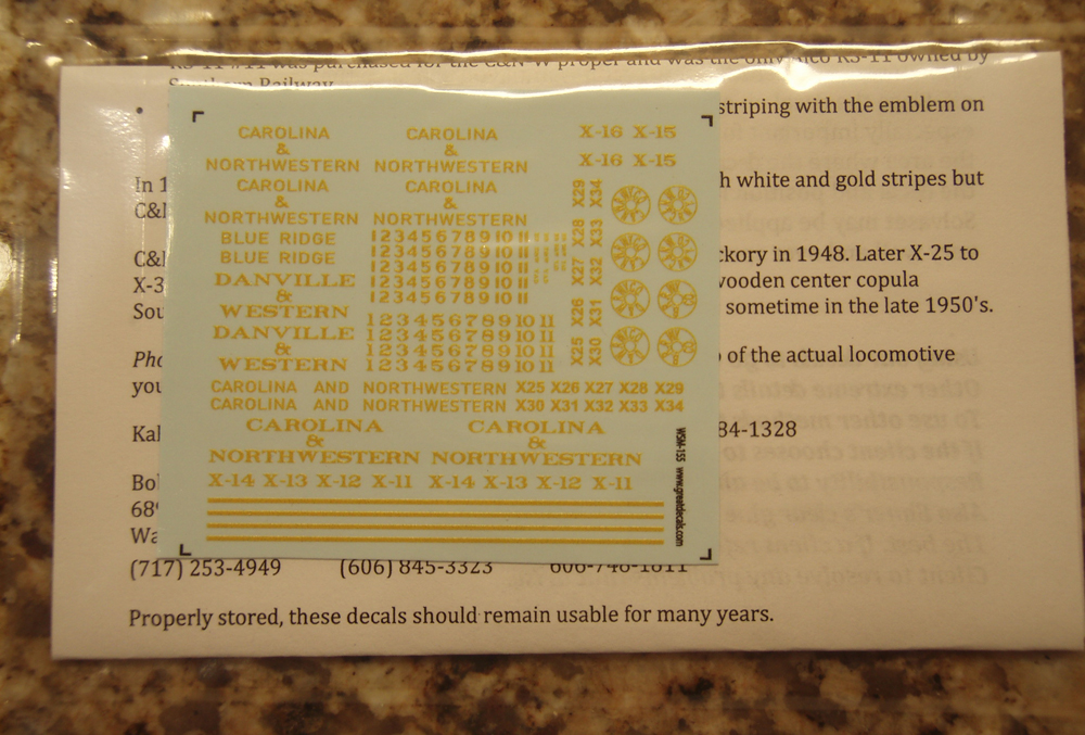 Photo of decal sheet with yellow graphics in clear plastic back with instruction sheet.