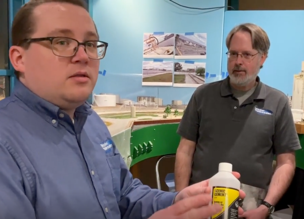 Two men near a model railroad layout, talking.