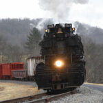 Nose of black steam locomotive and train coming around a bend