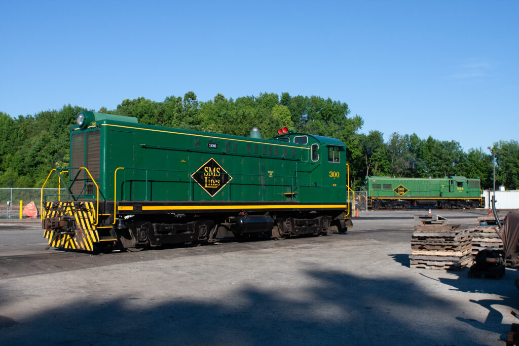 Two green locomotives in industrial yard.