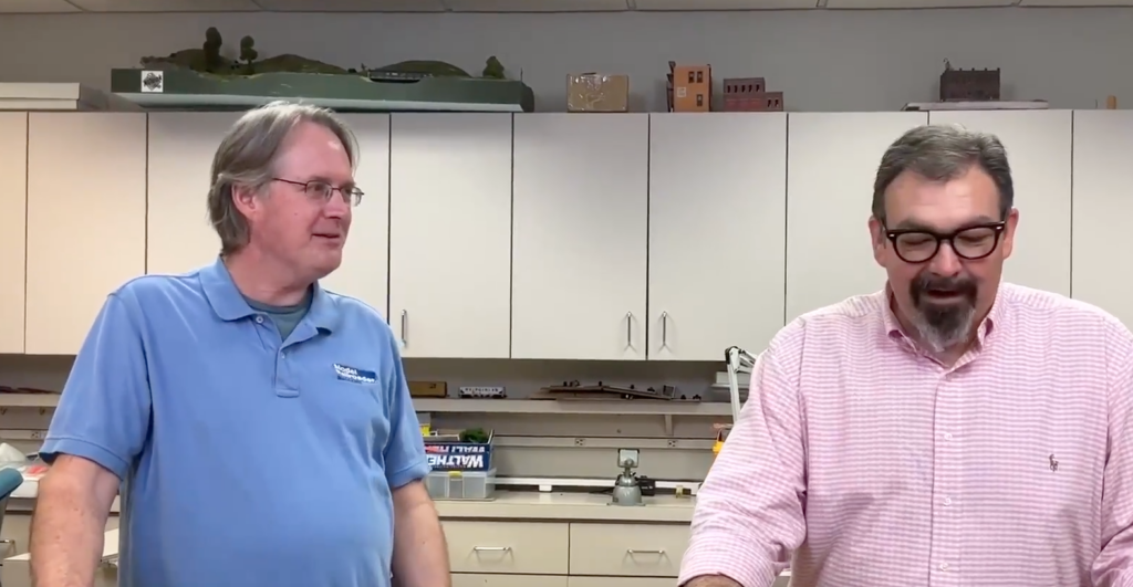 Two men speaking at a counter.