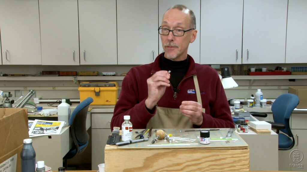 David Popp holding an N scale grade crossing signal at his workbench