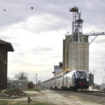 Passenger train passes grain elevator and closed interlocking tower