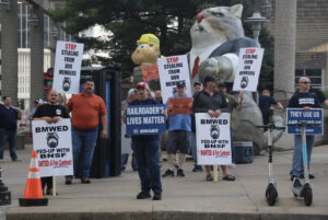 People holding signs while standing on sidewalk