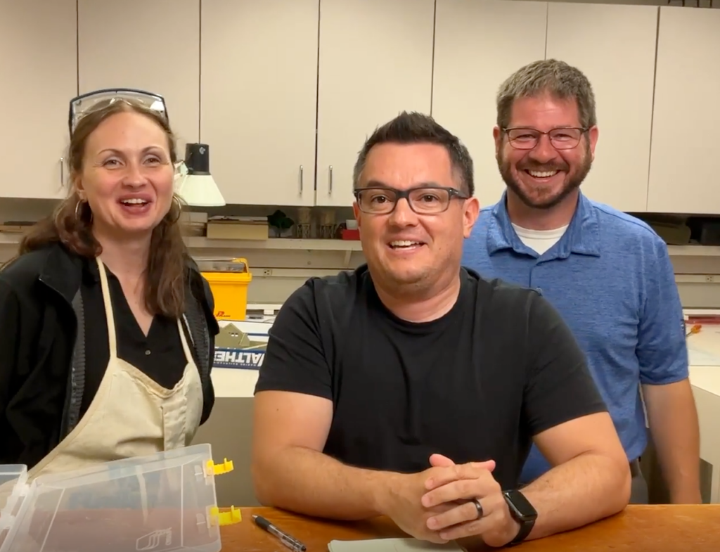 Three people standing behind a workbench.